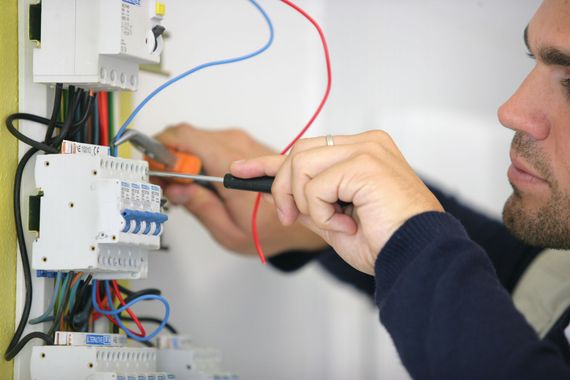 Un électricien utilise un tournevis et une pince pour ajuster les fils à l'intérieur d'un tableau électrique.