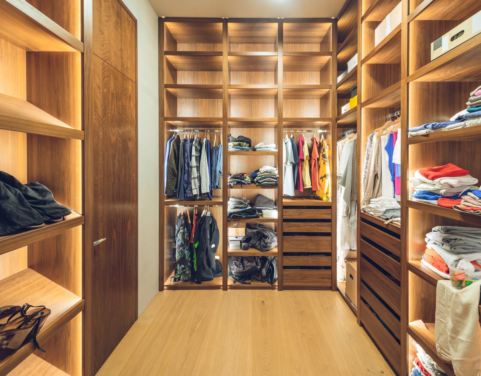 Un dressing avec des étagères en bois chaleureux, un éclairage à LED intégré, des vêtements suspendus et des vêtements pliés.