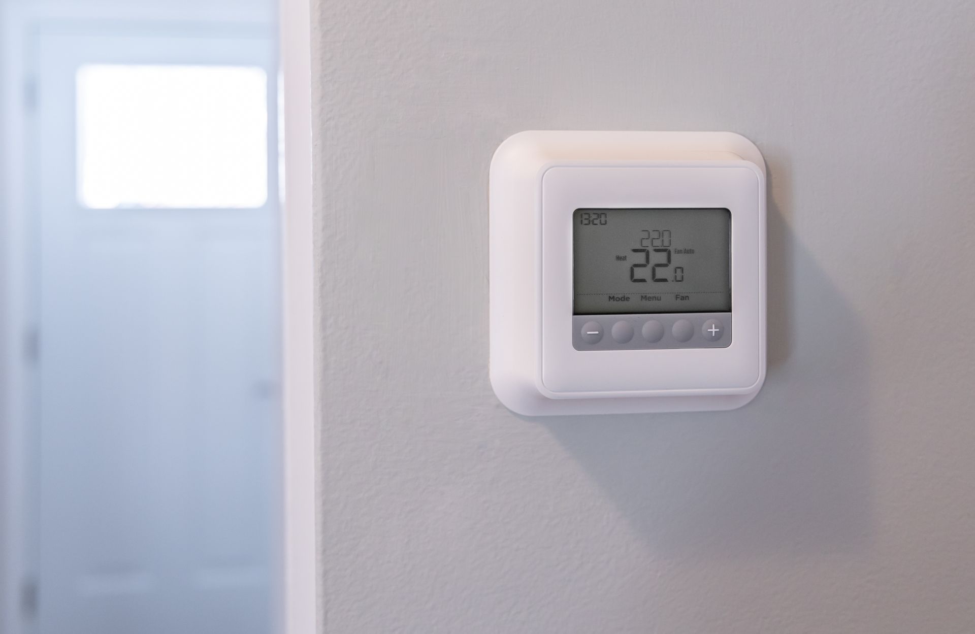 Un thermostat numérique, fixé sur un mur, affiche une température de 22 degrés Celsius.