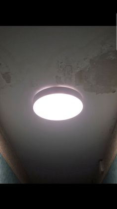 Un plafonnier circulaire encastré, lumineux, éclaire un plafond présentant quelques dommages superficiels visibles.