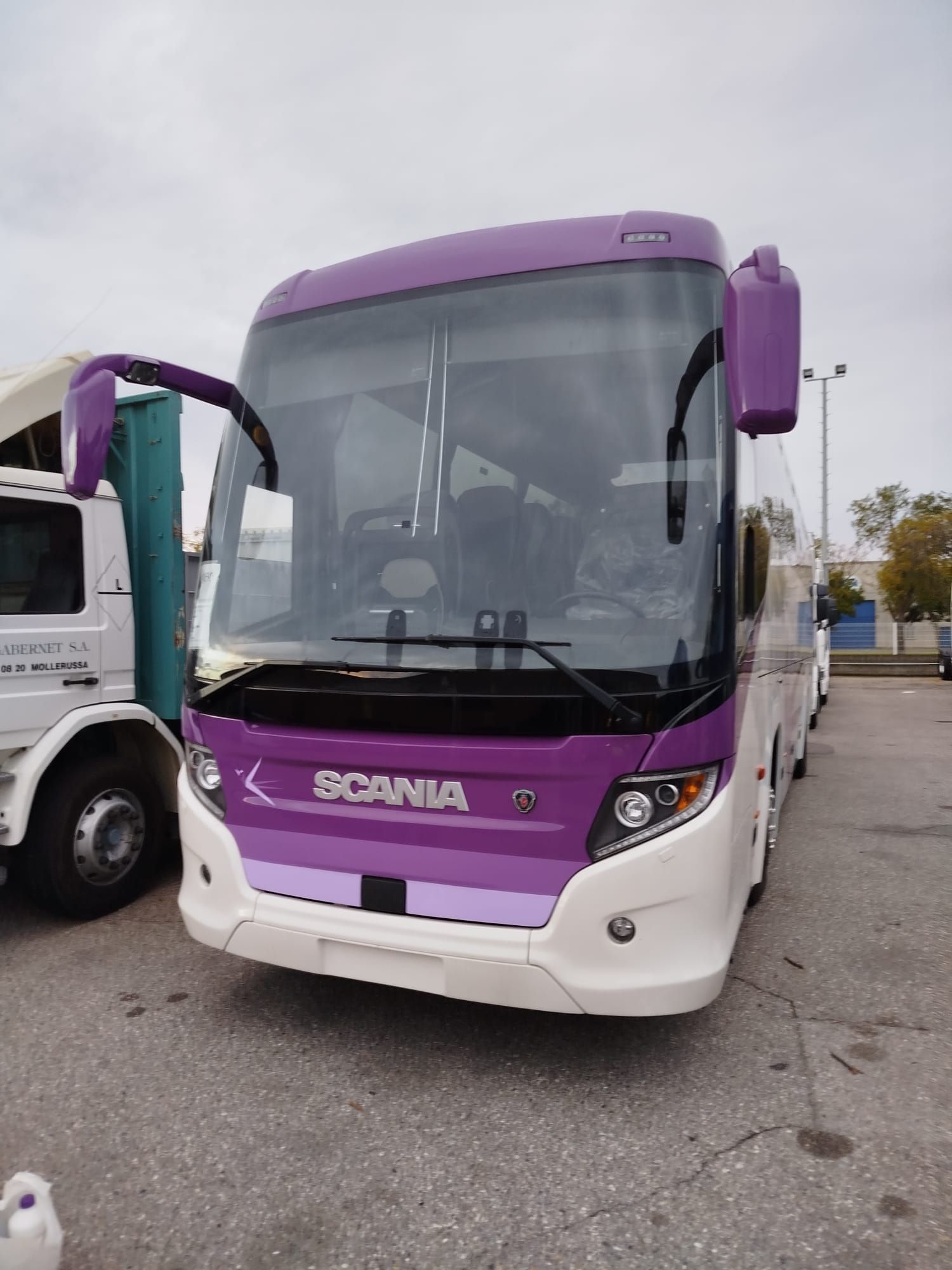 Un autobús Scania morado y blanco está estacionado en un estacionamiento.