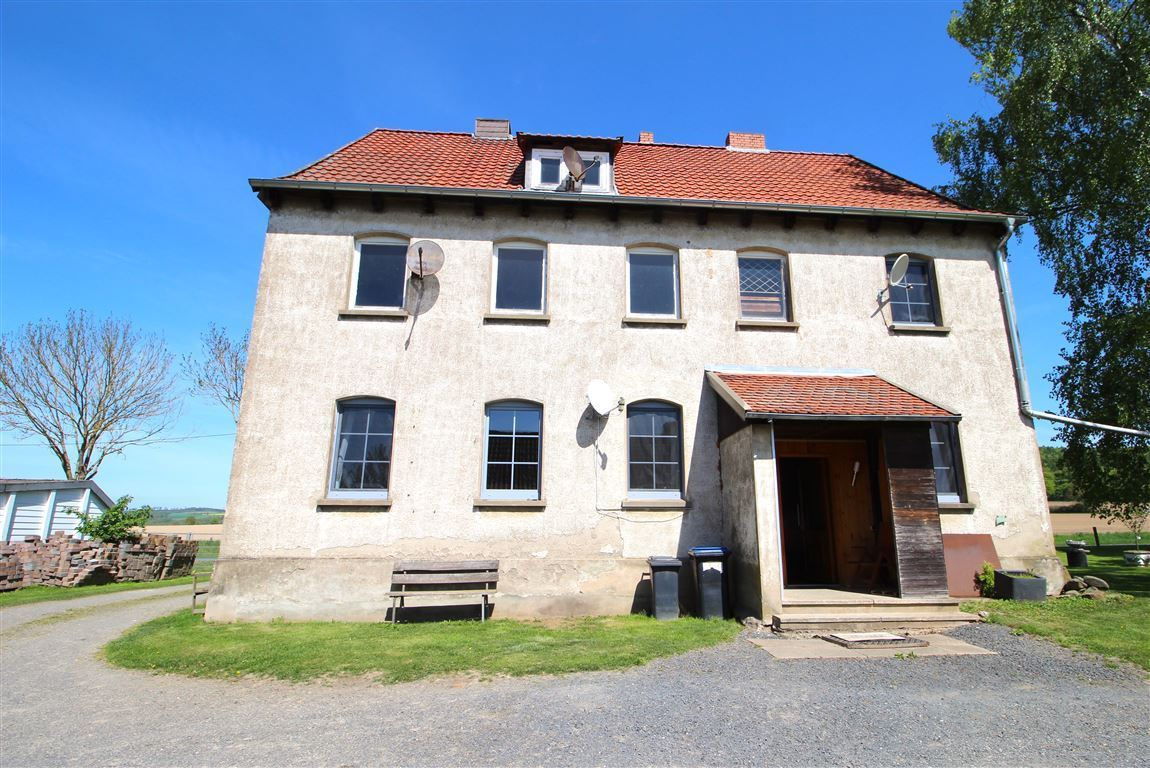 Two-story beige building with a red tiled roof under a blue sky, with a dark wooden door and windows.
