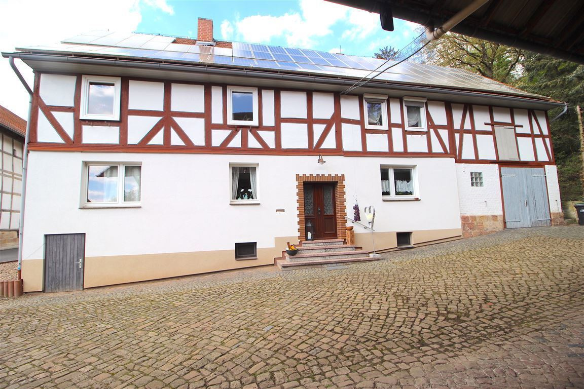 Two-story timber-framed house with white walls, brown beams, and solar panels on the roof.