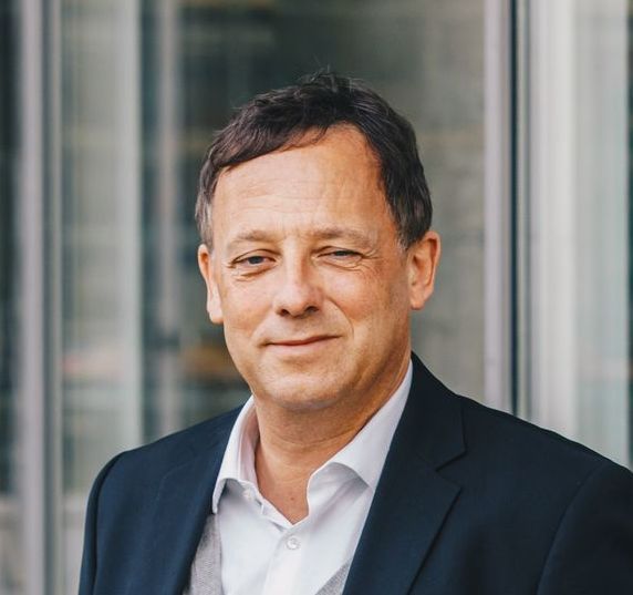 Ein Mann in Anzug und weißem Hemd lächelt in die Kamera.