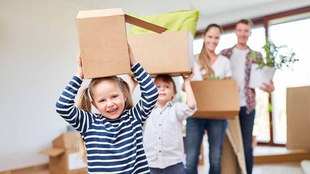 Eine Familie zieht in ein neues Zuhause und trägt Kisten auf dem Kopf.