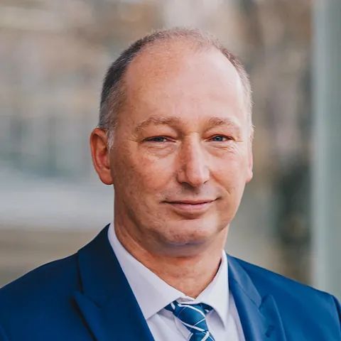 Ein Mann in Anzug und Krawatte lächelt in die Kamera.