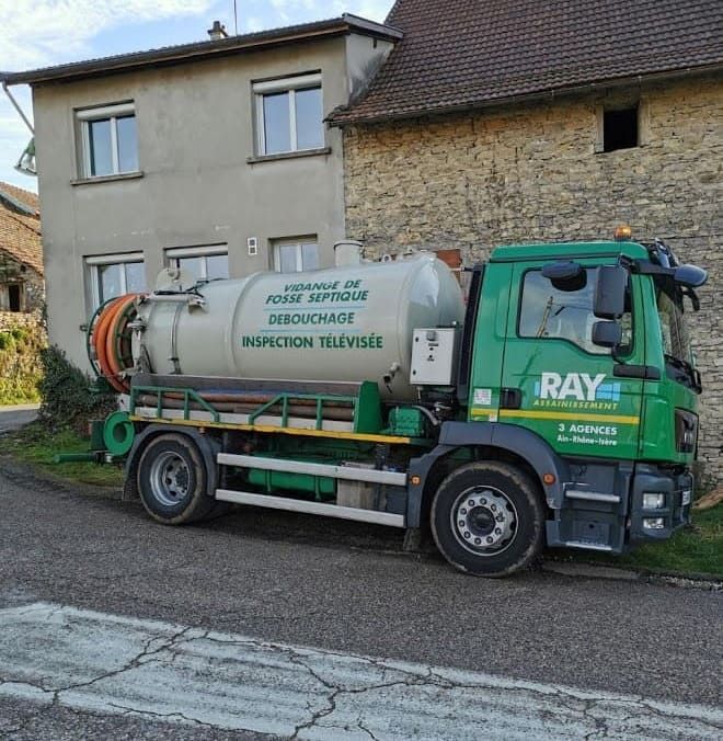 Un camion-citerne vert est stationné devant un bâtiment de couleur claire.