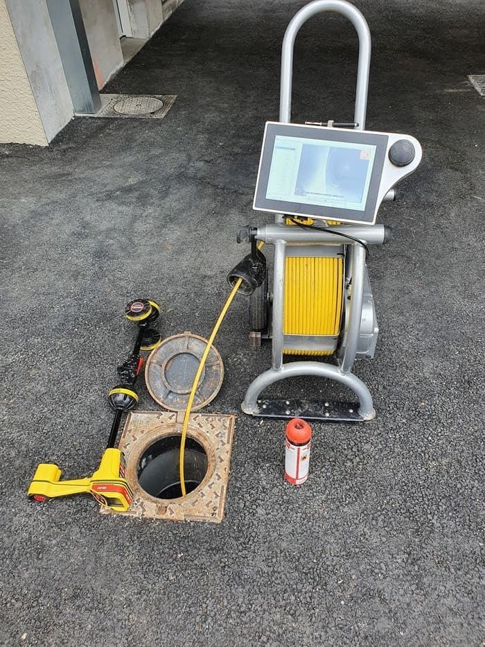 Équipement d'inspection des égouts installé sur la chaussée : caméra rotative, moniteur, plaque d'égout, robot d'inspection des canalisations et petite bouteille orange.