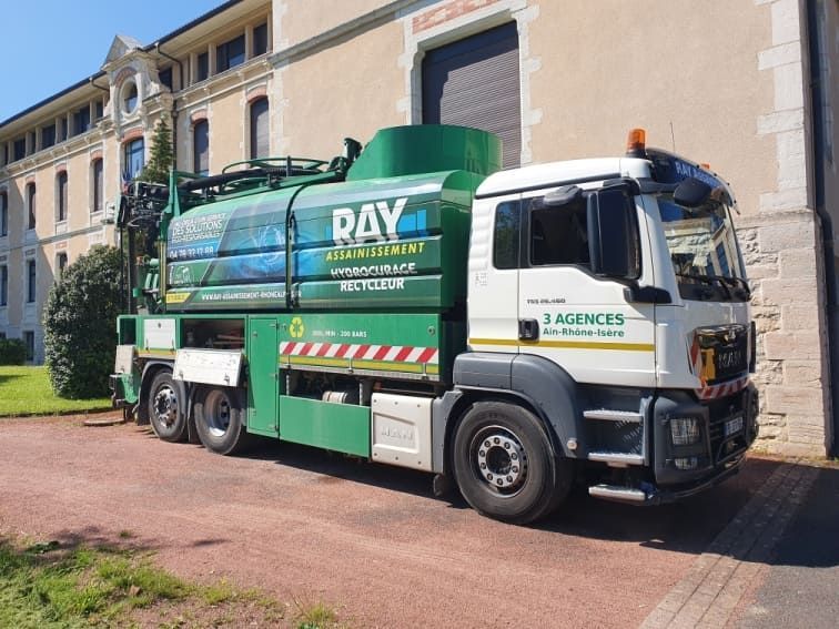 Camion de ramassage des ordures vert et blanc stationné devant un bâtiment clair. Logo Ray Assainissement .