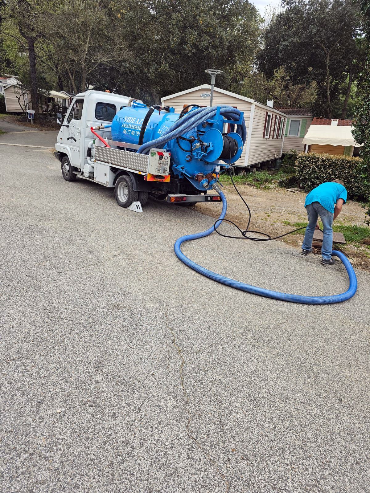 Une personne en train d'utiliser un long tuyau dans une canalisation derrière son véhicule d'assainissement.