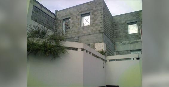 Extérieur d'un bâtiment en béton avec fenêtres barricadées, plantes et murs blancs.