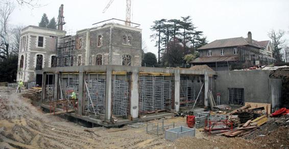 Chantier : ancien manoir en rénovation, avec échafaudages, ouvriers et supports en béton.