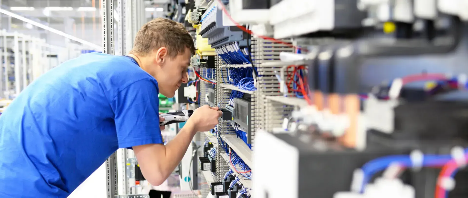 Ein Mann in einem blauen Hemd arbeitet in einer Fabrik an einer Maschine.