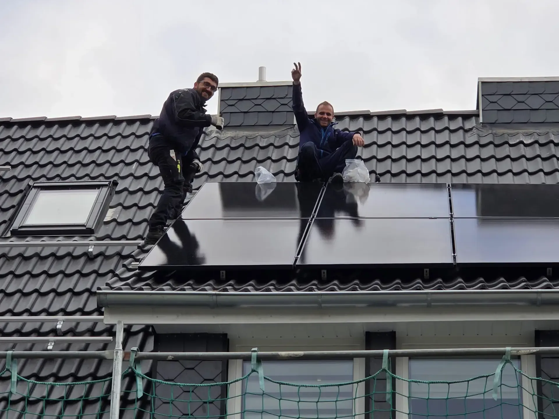 Zwei Männer installieren Solarmodule auf dem Dach eines Hauses.