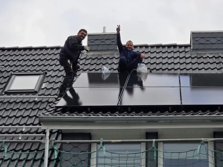 Zwei Männer installieren Solarmodule auf dem Dach eines Hauses.