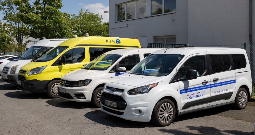 Auf einem Parkplatz vor einem Gebäude steht eine Reihe Transportwagen.