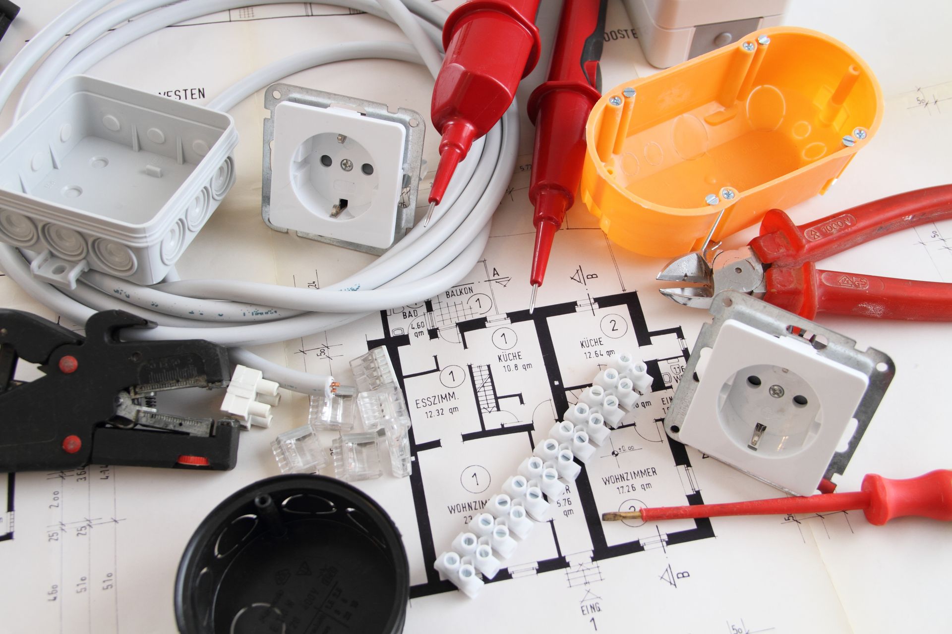Des composants électriques, des outils et un tournevis rouge sont disposés sur un plan de maison imprimé.
