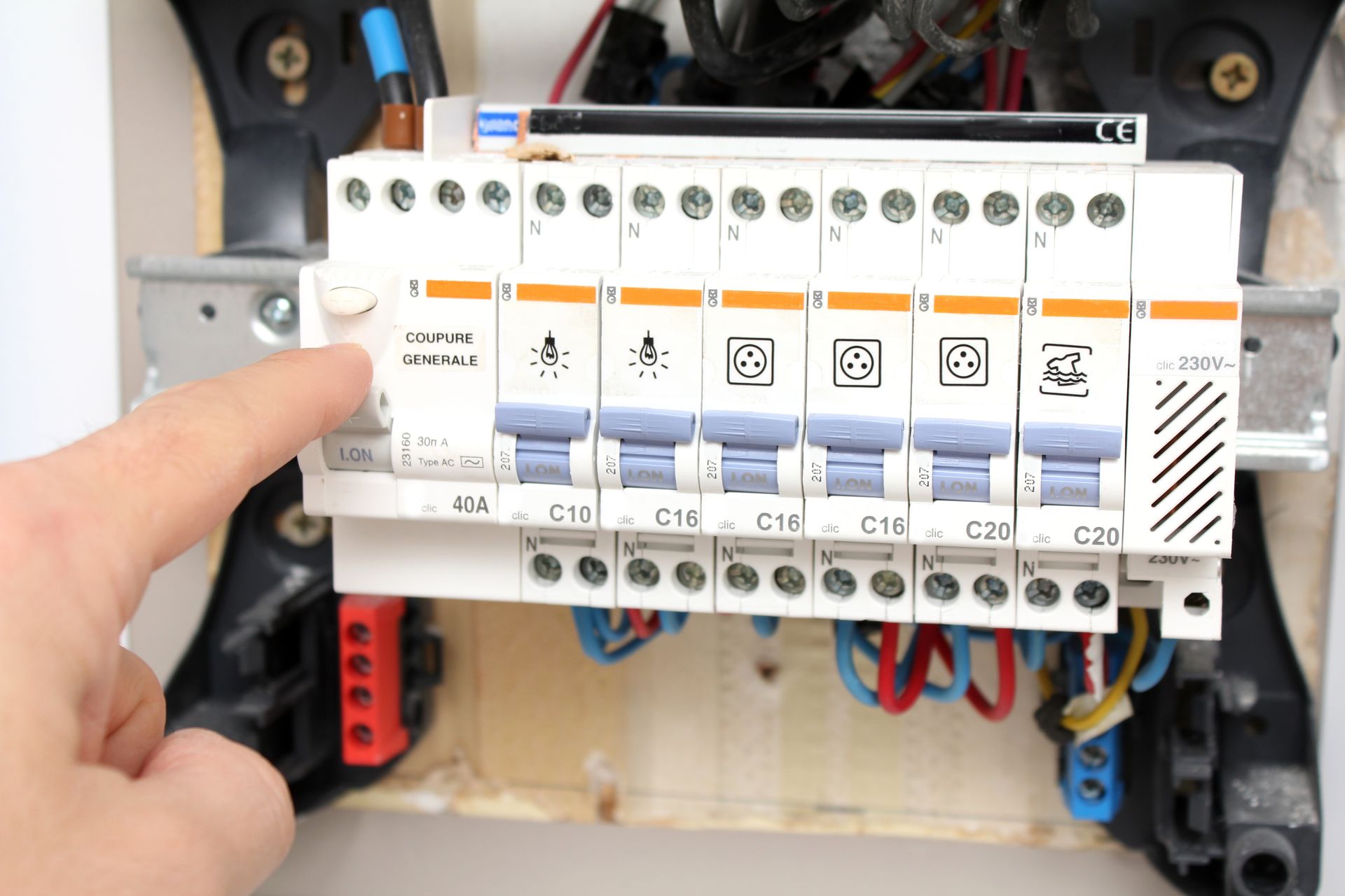 Une main actionne un interrupteur sur un tableau électrique, qui comporte plusieurs disjoncteurs avec des icônes.