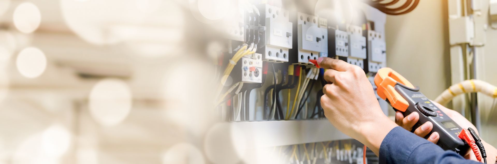 Un technicien utilise une pince ampérométrique numérique pour tester les composants électriques à l'intérieur d'un tableau de disjoncteurs.