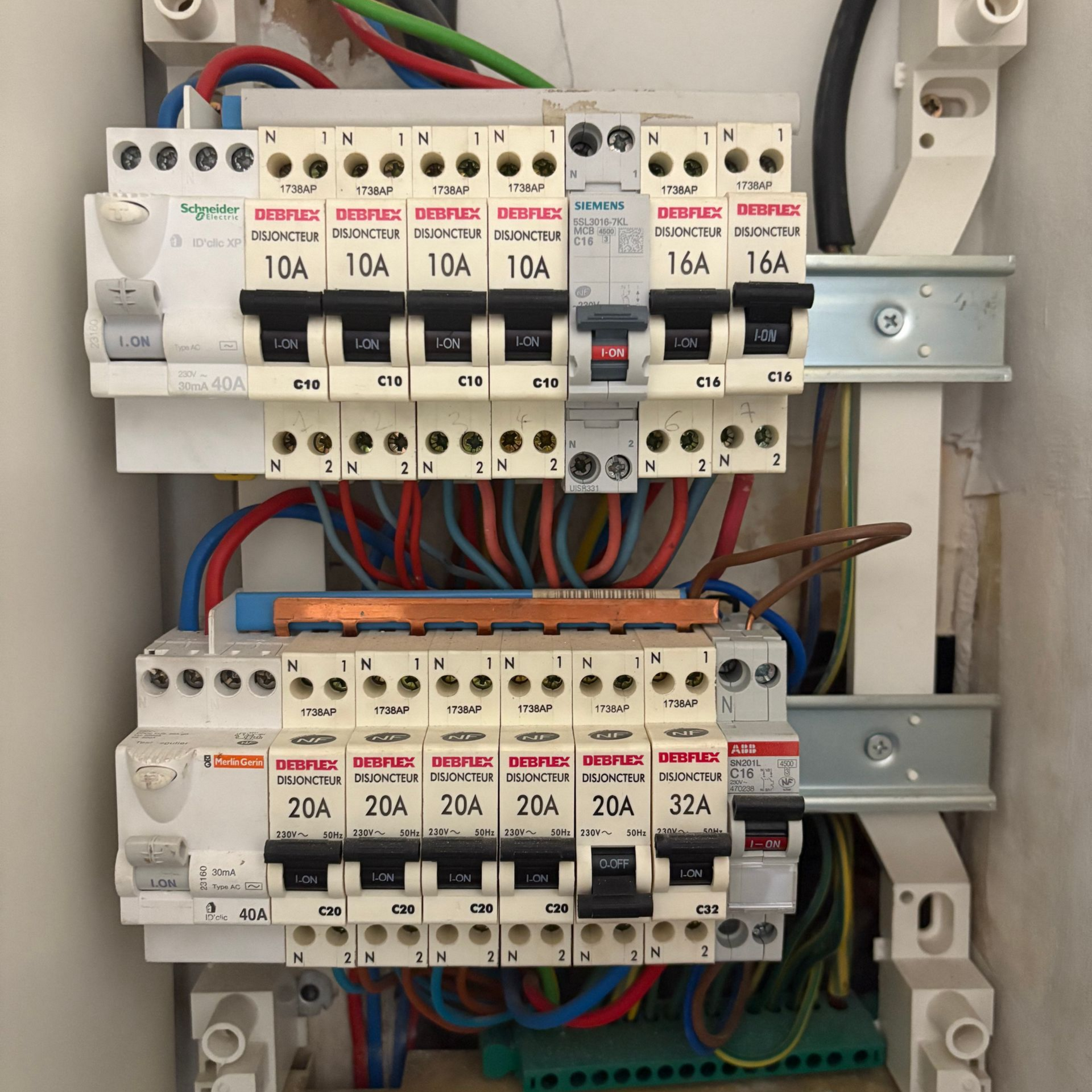 Deux rangées de disjoncteurs électriques montées sur un rail DIN à l'intérieur d'un tableau de distribution résidentiel.
