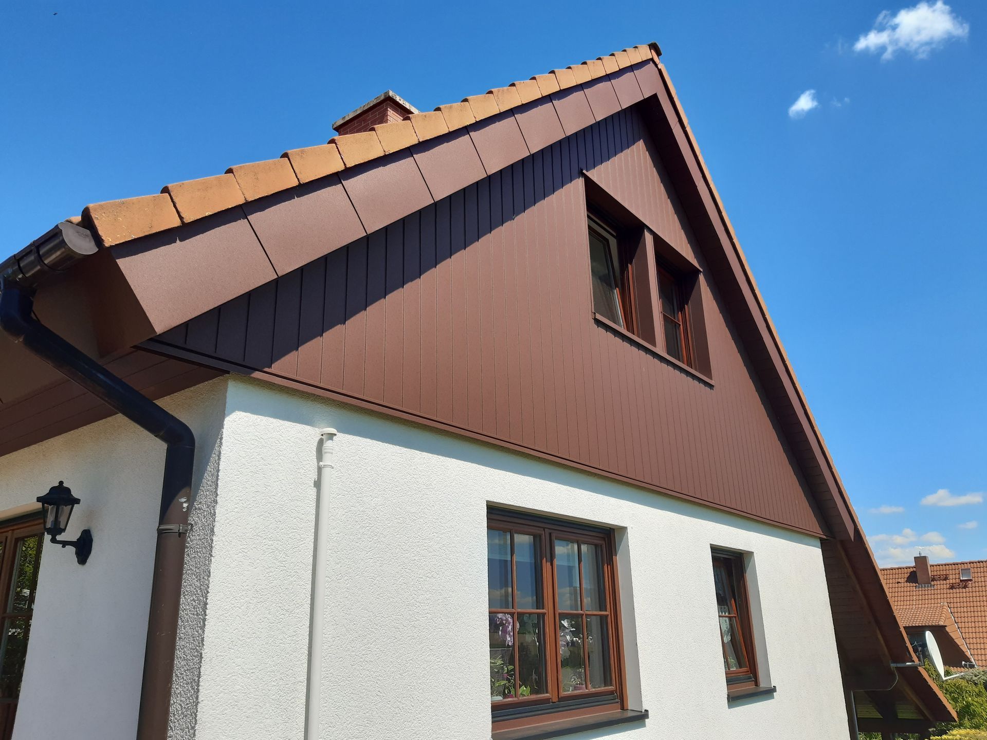 Holzchalet mit Balkon und Bergen im Hintergrund, unter einem teilweise bewölkten Himmel