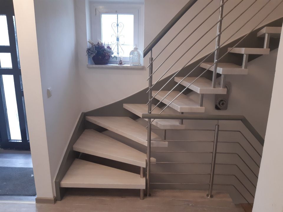 Moderne Innentreppe mit weißen Stufen, Metallgeländer und einem kleinen Fenster im Treppenabsatz