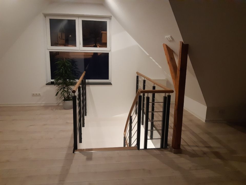 Innentreppenhaus mit hellem Holzboden, schwarzem Geländer und einem Fenster im Treppenabsatz
