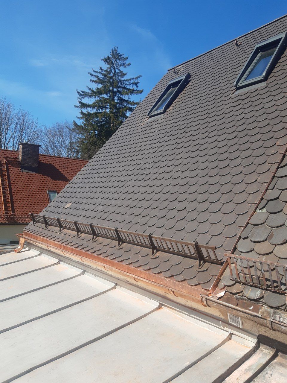 Dach mit grauen Schindeln, Oberlichtern und einer weißen Metallmarkise unter klarem, blauem Himmel