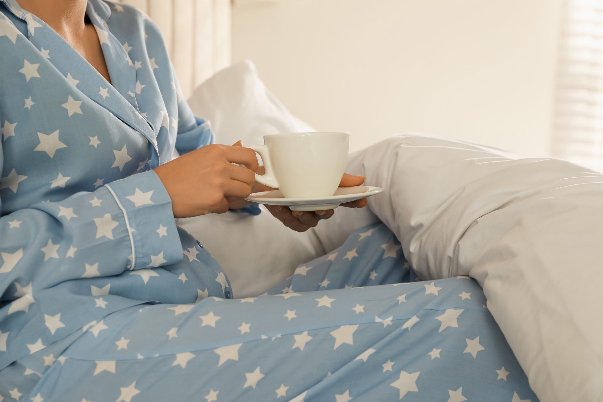 Una mujer en pijama está sentada en una cama sosteniendo una taza de café.