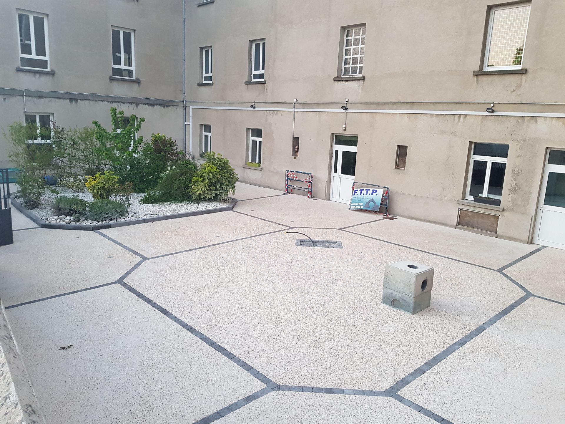 Cour d'immeuble réaménagée avec sol drainant clair, bordures décoratives géométriques, espaces végétalisés et regard technique permettant l'accès aux réseaux souterrains.