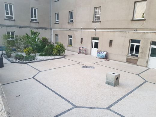 Cour d'immeuble réaménagée avec sol drainant clair, bordures décoratives géométriques, espaces végétalisés et regard technique permettant l'accès aux réseaux souterrains.
