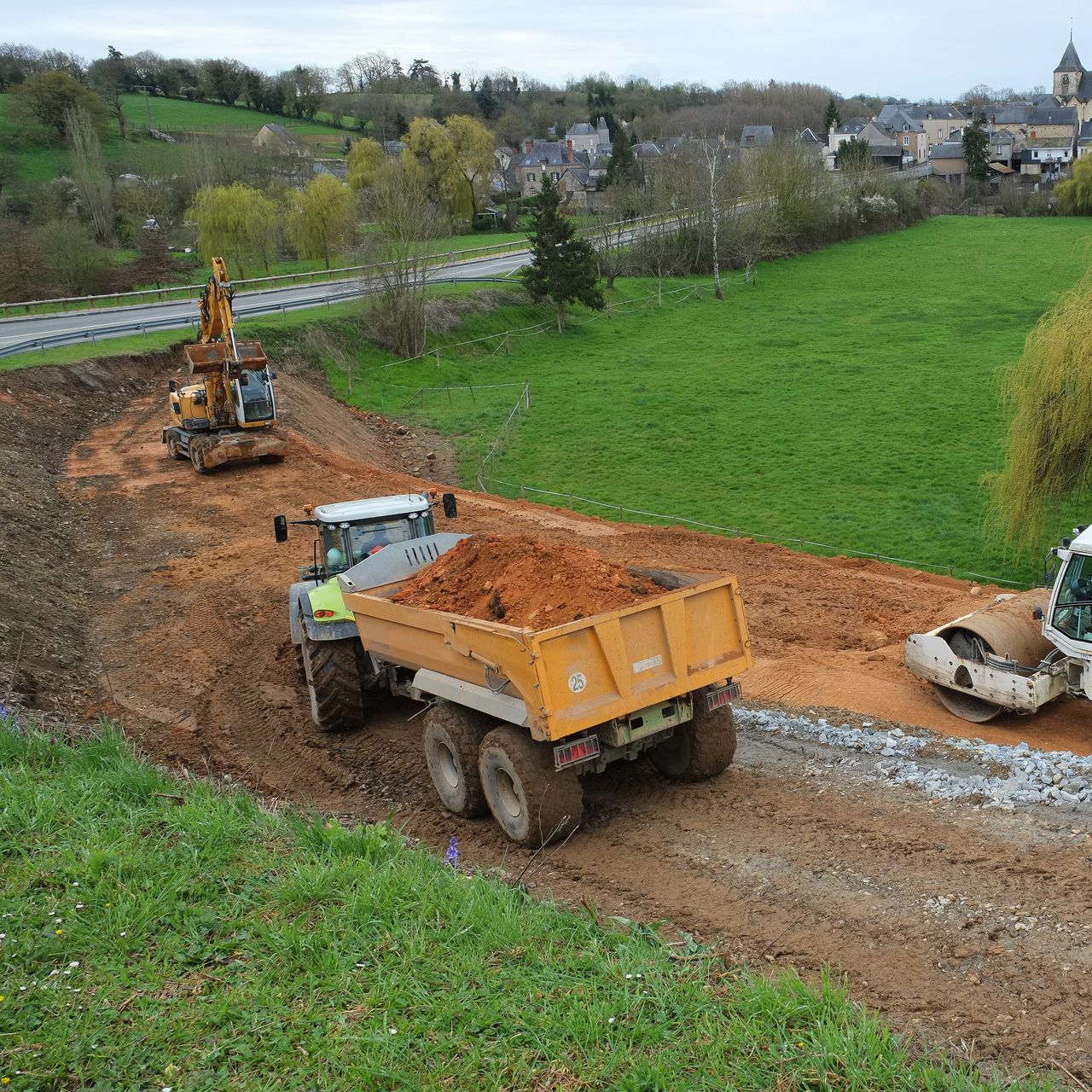 Des camions-bennes transportent de la terre sur un chemin rural.