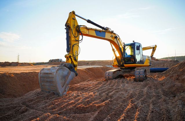 Une pelleteuse jaune creuse la terre sur un chantier de construction au coucher du soleil.
