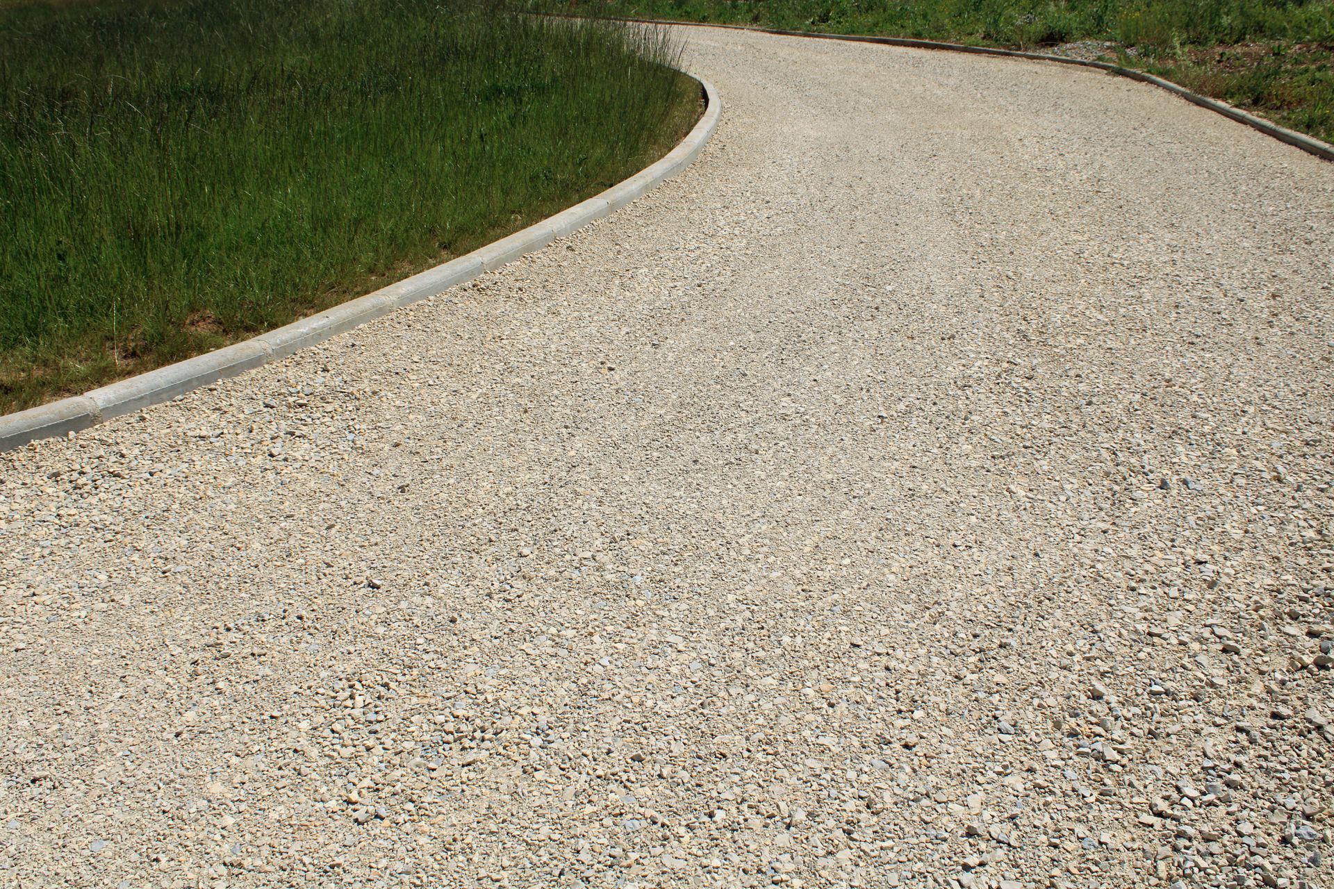 Chemin de gravier sinueux bordé de gazon vert.