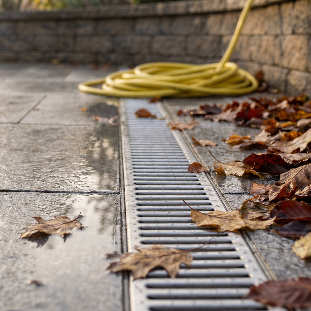 
Caniveau de drainage extérieur avec grille métallique et feuilles mortes.