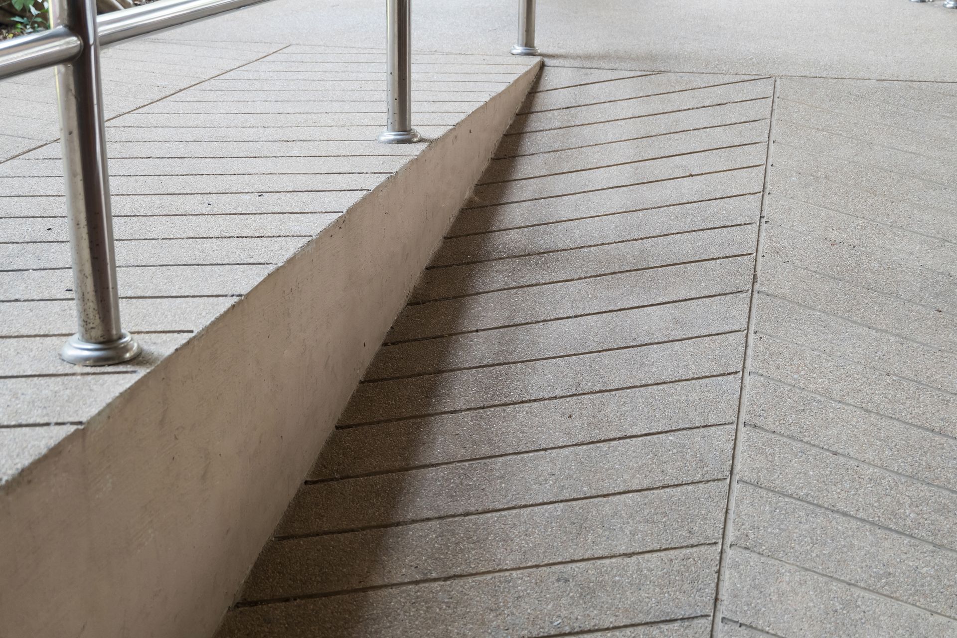 Rampe d'accès accessible bordée de garde-corps métalliques, réalisée en revêtement drainant pour assurer l'évacuation des eaux de pluie.