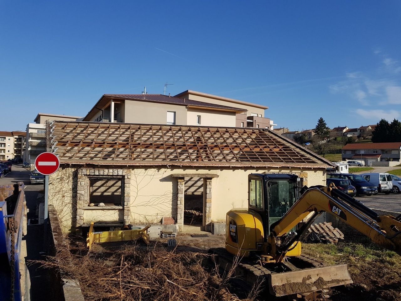 Petite maison en démolition avec une pelleteuse au premier plan.