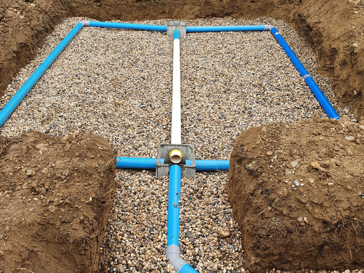 Système de drainage composé de canalisations et de regards de répartition installés dans une fouille avec lit de graviers.