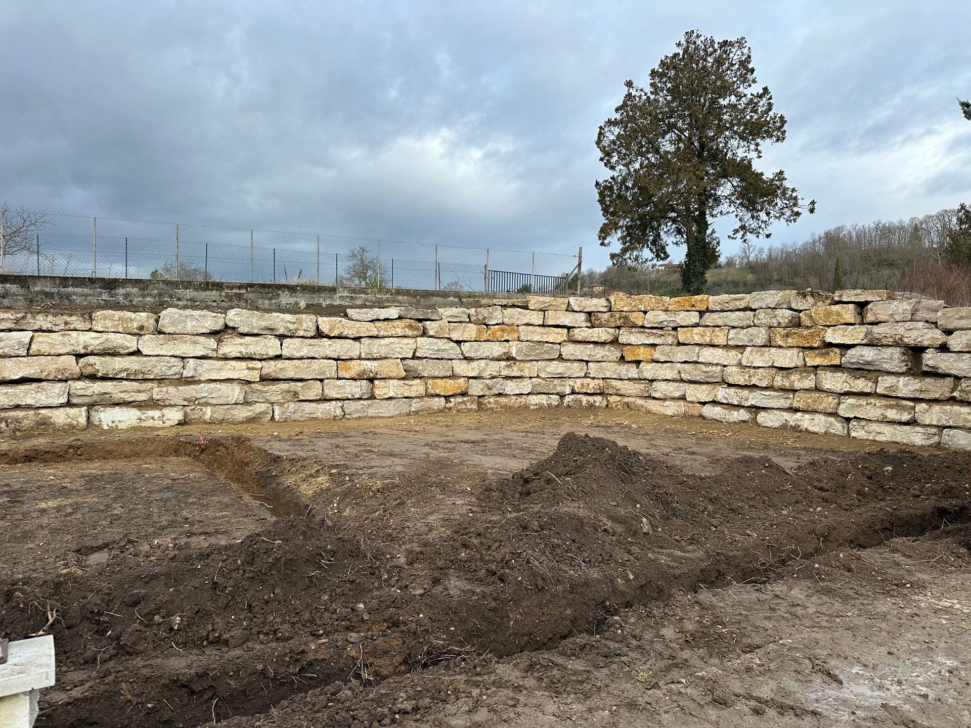 Mur de soutènement en pierre sous un ciel nuageux, à côté d'un terrain en cours de terrassement.