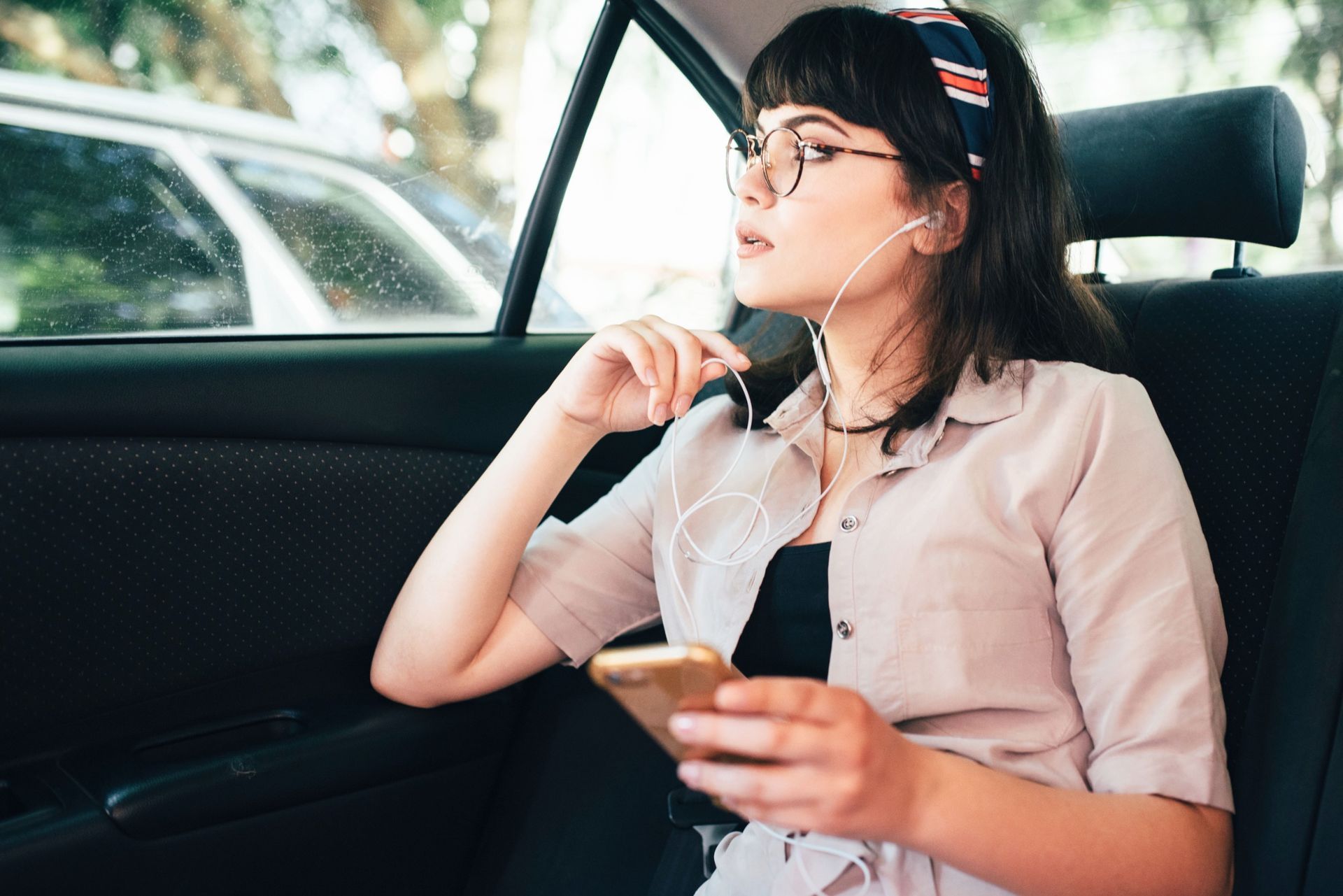 Una mujer está sentada en el asiento trasero de un automóvil escuchando música en su teléfono.