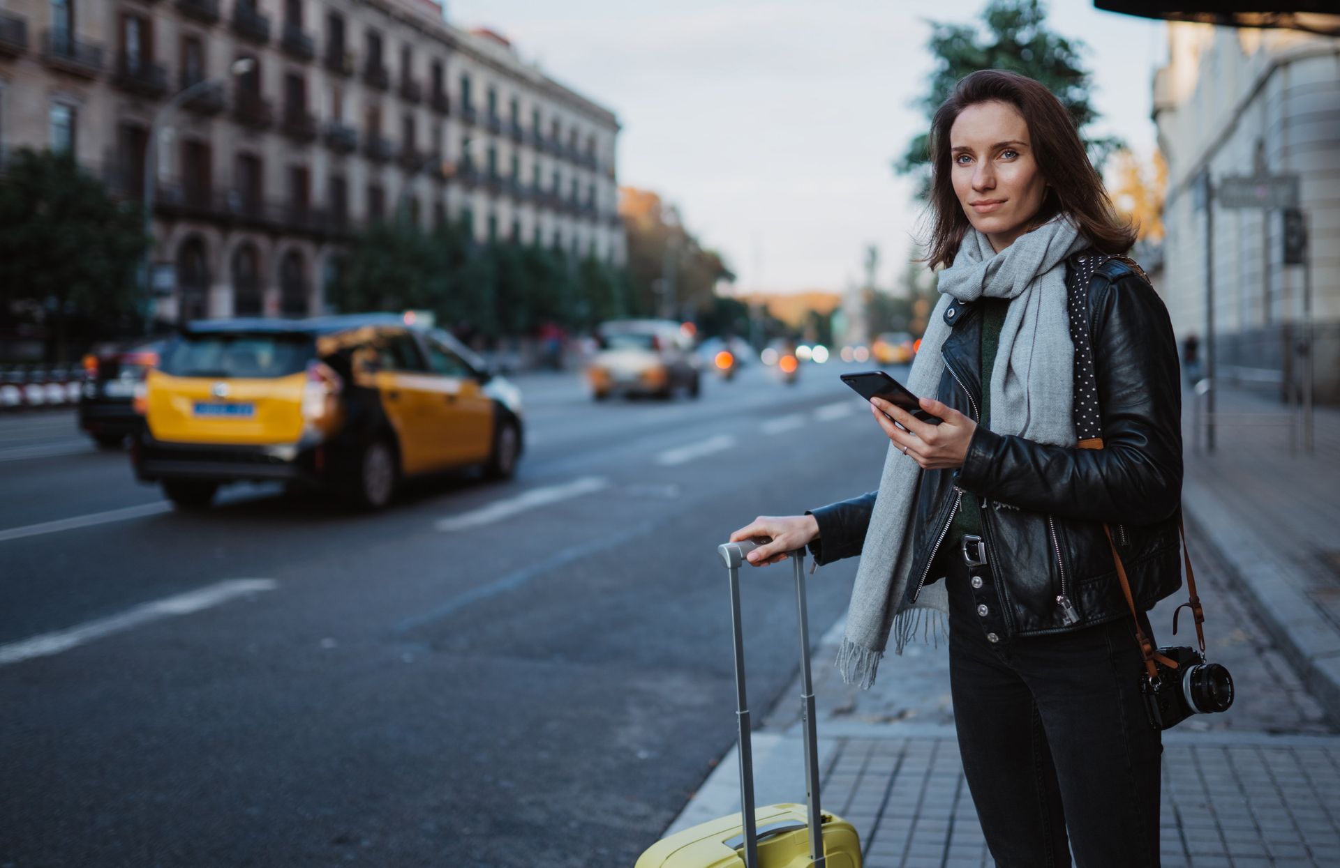 Una mujer sostiene una maleta amarilla y mira su teléfono.