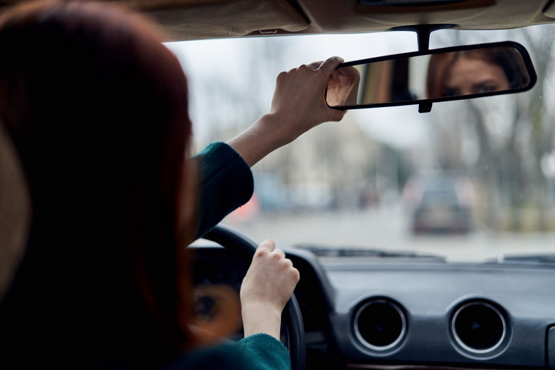 Una mujer está ajustando su espejo retrovisor mientras conduce un automóvil.