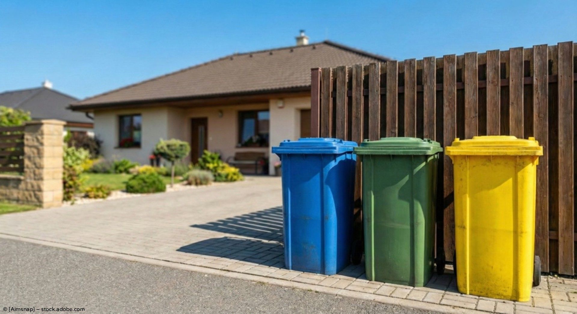 Drei farblich gekennzeichnete Recyclingbehälter vor einem Vorstadthaus entlang einer Einfahrt