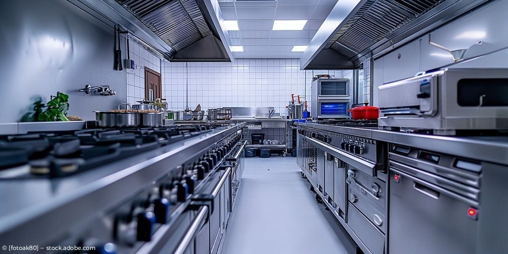 Moderne gewerbliche Küche aus Edelstahl mit langen Arbeitsflächen, Herden und Deckenlüftung.
