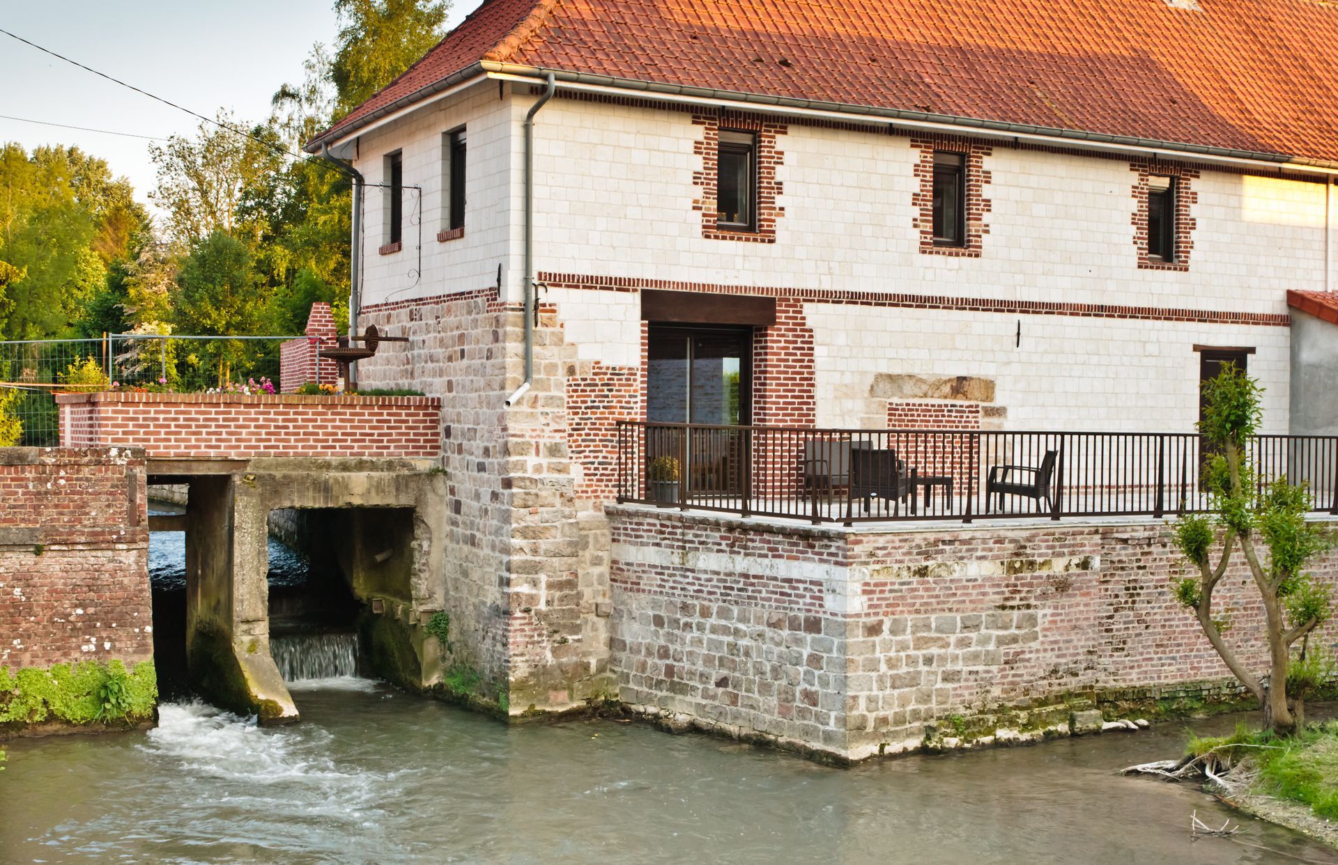 Bâtiment historique en briques et en pierres, traversé par un cours d'eau ; toit de tuiles rouges.