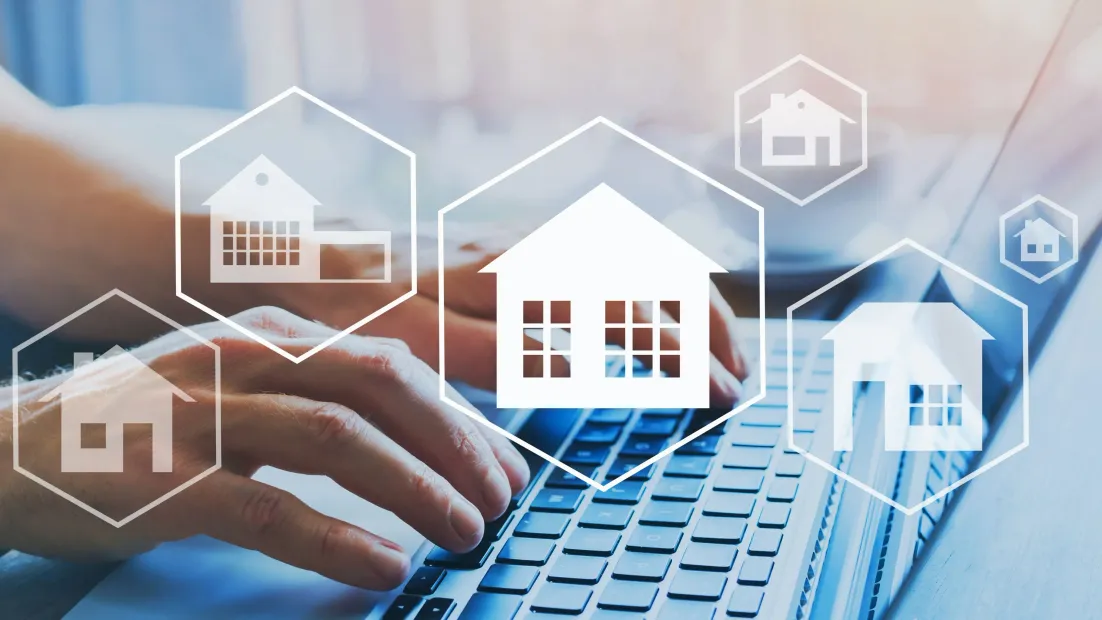 Persona que usa una computadora portátil con íconos de casas superpuestos, sugiriendo la búsqueda de bienes raíces o una vivienda.