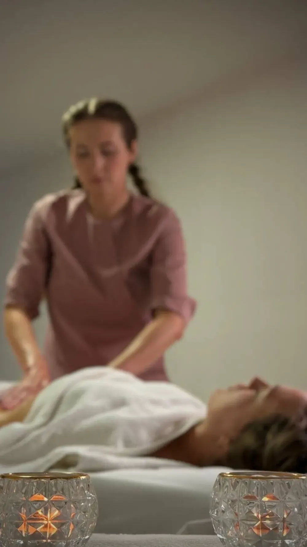 Una persona con una camisa rosa le da un masaje a alguien que está acostado, con dos velas encendidas en primer plano.