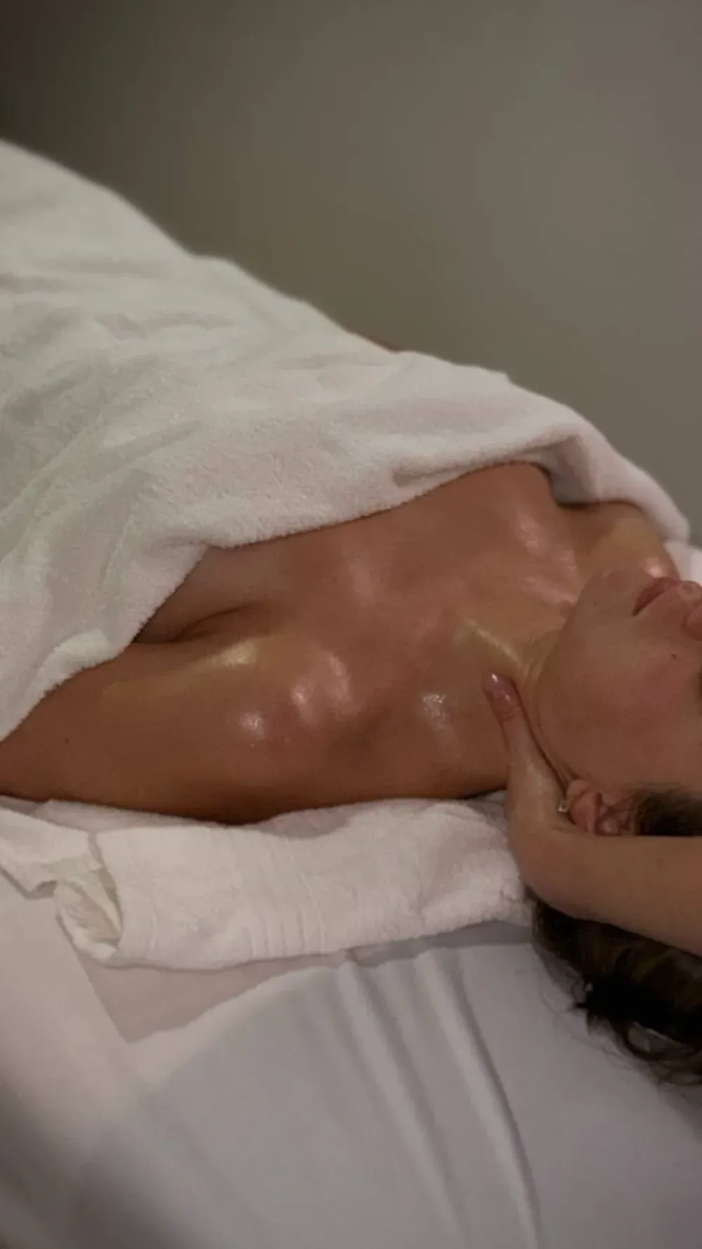 Una persona recibe un masaje profesional mientras está tumbada en una camilla de spa cubierta con toallas blancas.
