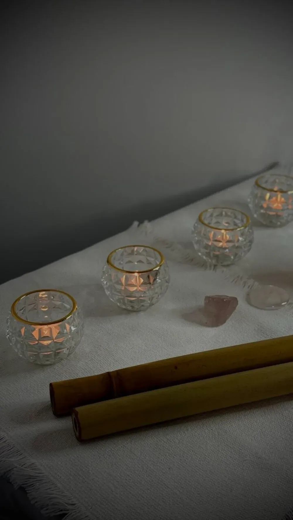 Varias pequeñas velas votivas de cristal brillan suavemente sobre una superficie blanca texturizada