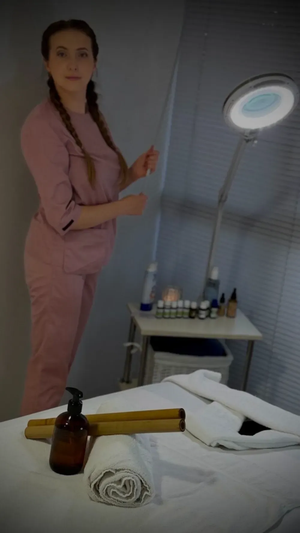 Una persona vestida con un uniforme quirúrgico rosa se encuentra en una sala de tratamiento junto a una lámpara de aumento